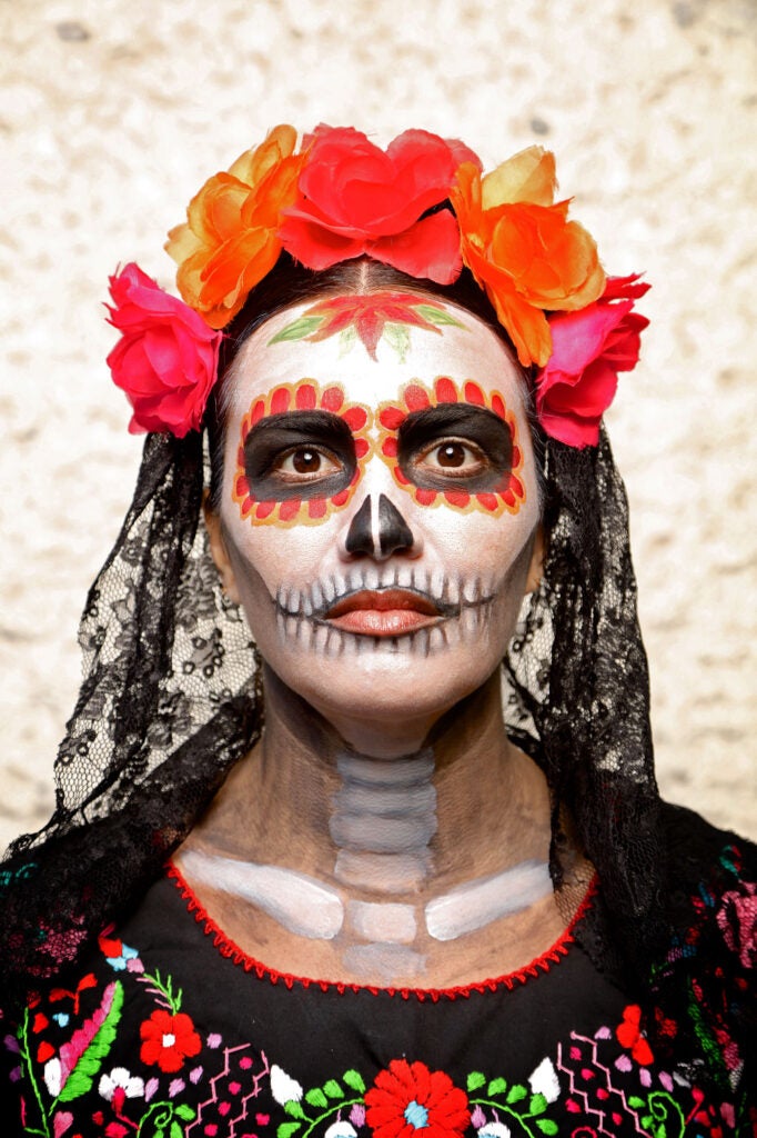 A women with a decorative painted face like a skeleton and a black embroidered shirt in honor of la Catrina