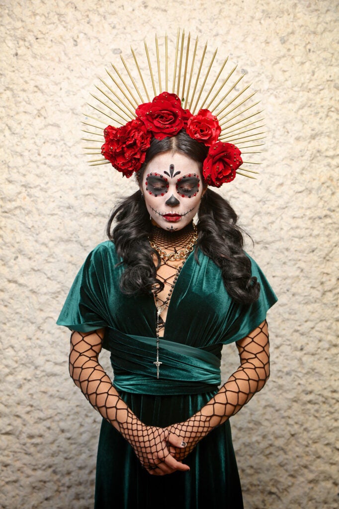 A women with a decorative painted face like a skeleton and a green dress in honor of la Catrina