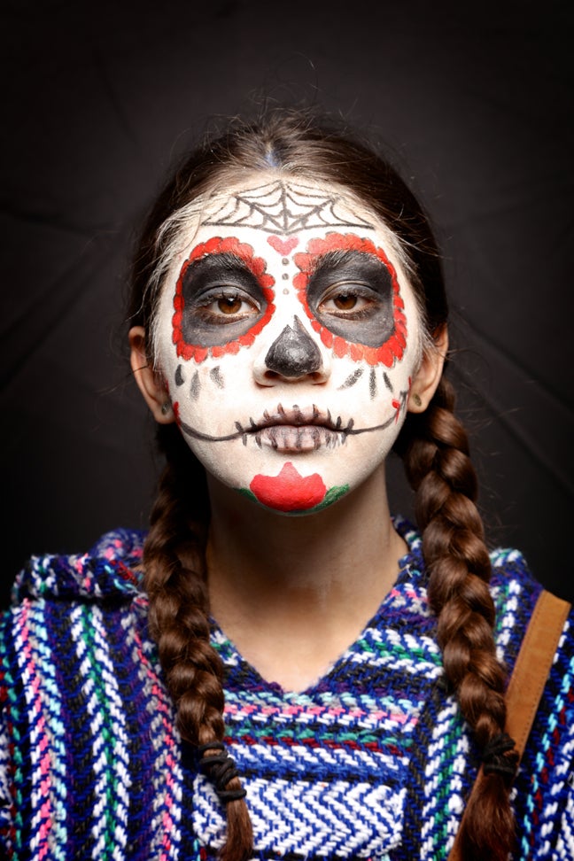 A women with a decorative painted face like a skeleton and a patterned shirt in honor of la Catrina