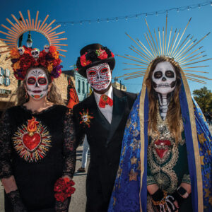 3 people dressed in traditional clothing to celebrate Dia de los Muertos.