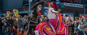 Two people dressed in traditional clothing dancing during the Dia de los Muertos parade.