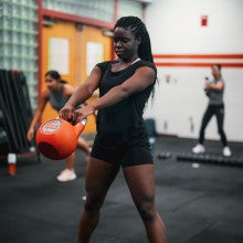 Woman swinging orange kettle bell. 