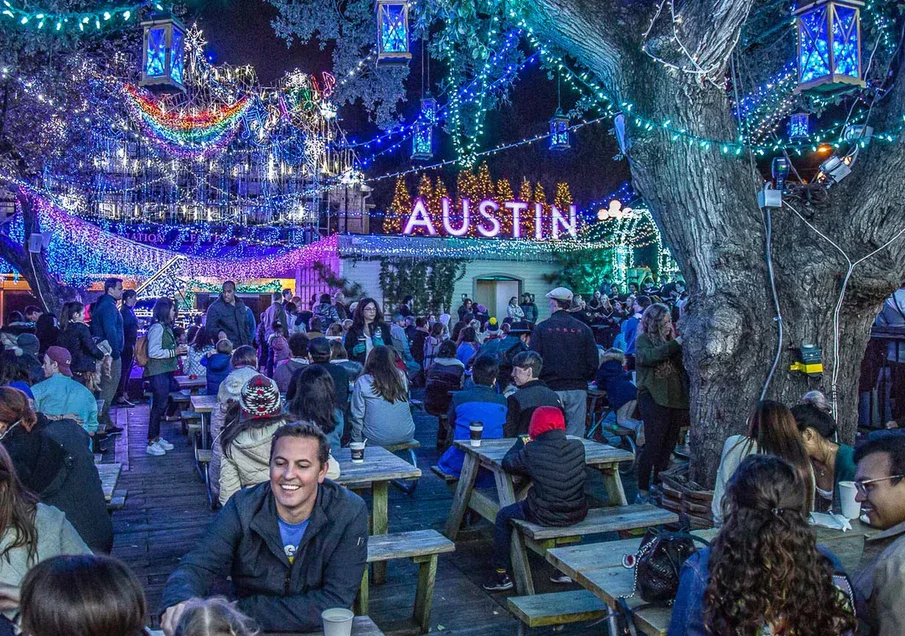 Mozart's coffee, a popular coffee place in Austin, TX, is lit up and decorated for Christmas at night with groups of smiling people