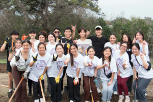 A group of smiling UT students holding up the UT hook'em hand sign while volunteering.