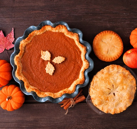 Delicious looking holiday pies are spread out on a table with small decorative pumpkins