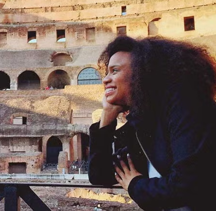 A female student stares out and smiles while visiting the Colusseum in Rome