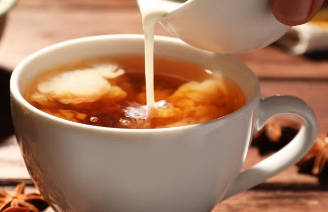 milk swirls as it is poured gently into a white hot tea cup