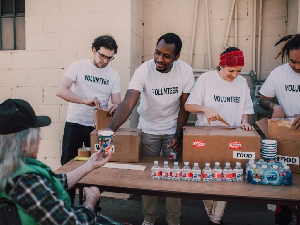 Volunterring and Community Service text is overlaid an image of volunteers packing items with a UT orange wash
