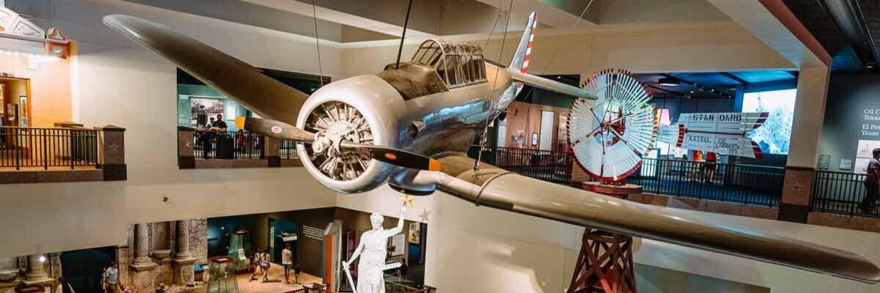 Vintage aircraft suspended in a museum with a propeller and a large rotor display in the background.