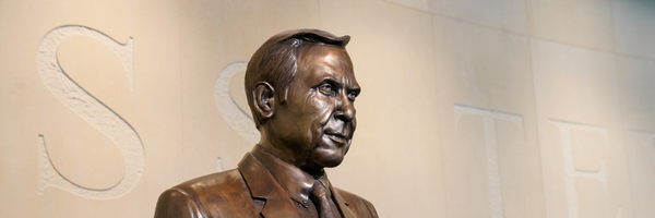 Bronze bust of a man against a beige wall with carved letters.