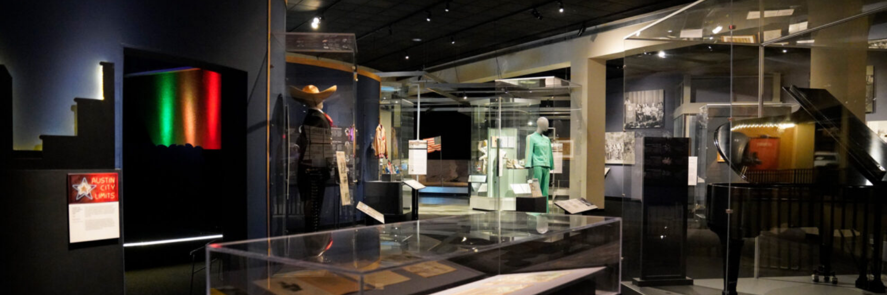 Interior of a museum exhibit with display cases, mannequins, and a grand piano.