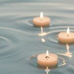 Five floating tea light candles on calm blue water with gentle ripples.