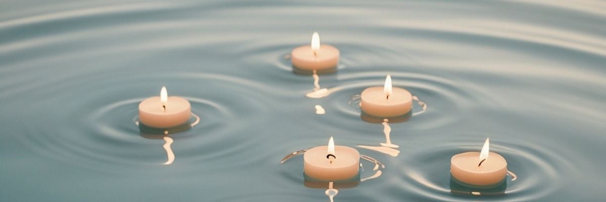 Five floating tea light candles on calm blue water with gentle ripples.