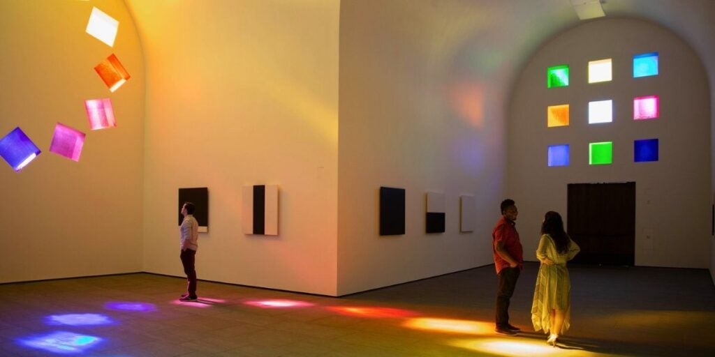 Visitors roam the building installation and art gallery known as the Austin by Ellsworth Kelly, as the colorful stained glass windows cast vivid light on the floor.