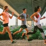 Five people jogging under a bridge on a gravel path, surrounded by greenery. They appear focused and energetic, conveying a sense of fitness and determination.