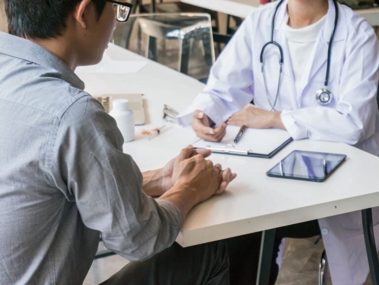A student consults with a doctor at a table. A tablet and clipboard are present.