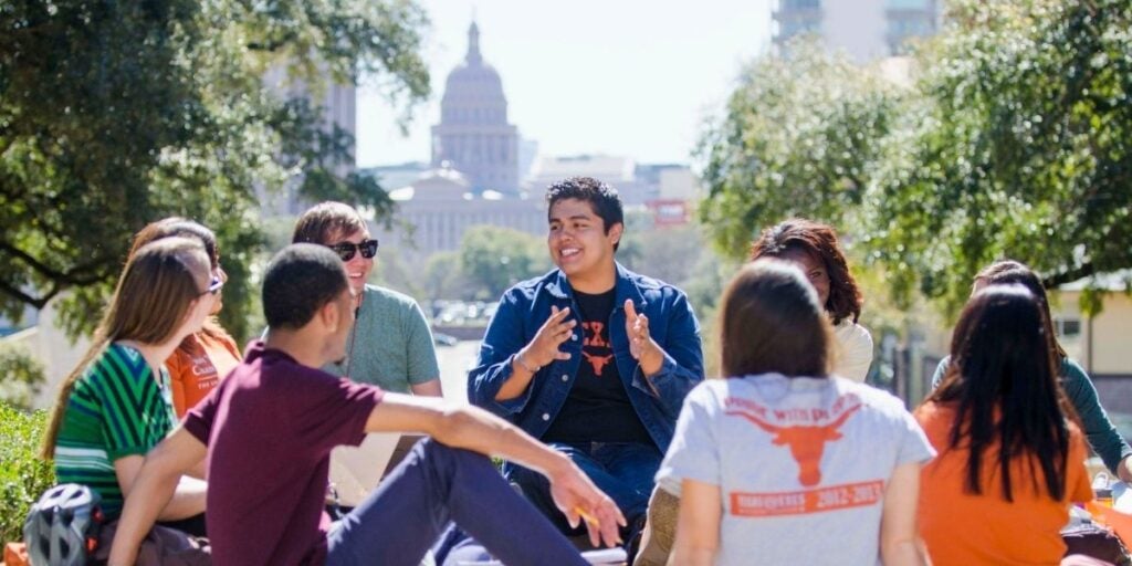 A group of people sitting in a circle outdoors, with a capitol building visible in the background.