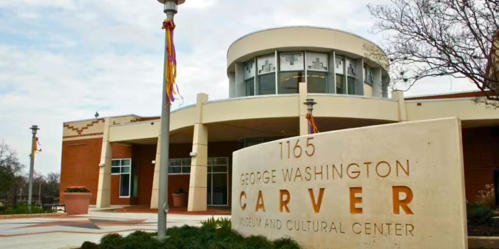 The entrance to the George Washington Carver Museum and Cultural Center, featuring a modern brick and cream façade with large windows and a sign in front.