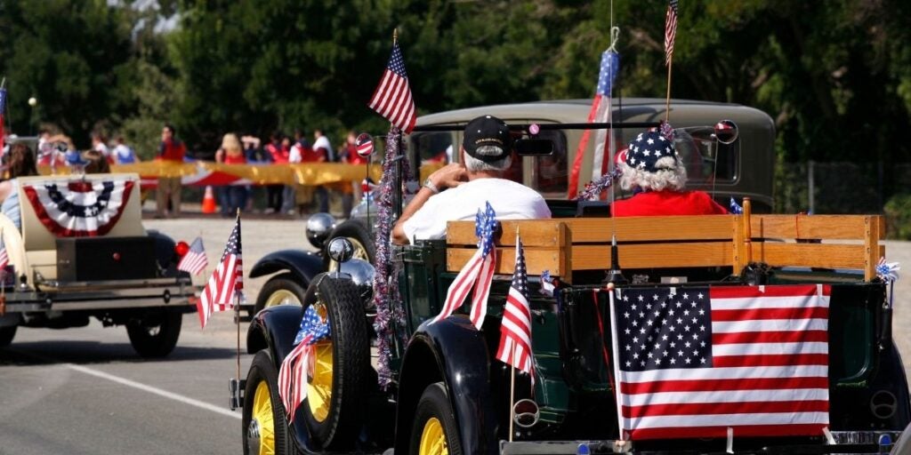 Vintage cars decorated with American flags in a parade, with spectators in the background.