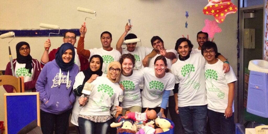 A group of eleven people in matching white T-shirts holding paint rollers and brushes, posing cheerfully.
