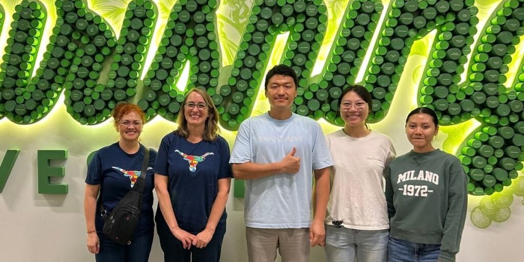 Five people standing in front of a green decorative wall with cylindrical shapes forming letters.